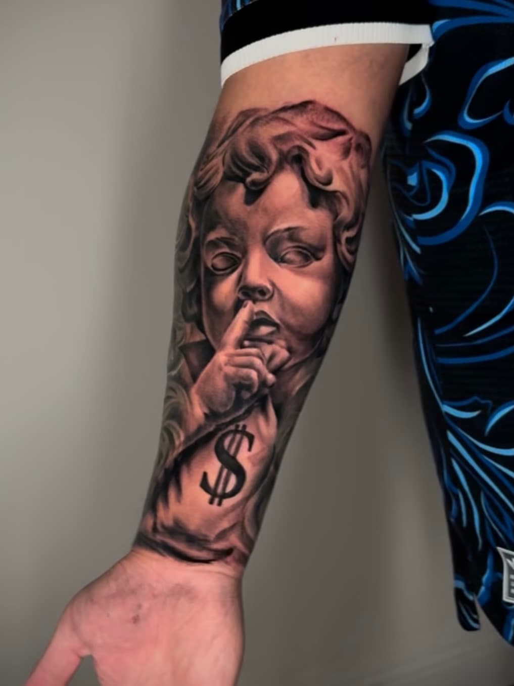 Forearm piece in black and grey — a cherub with a finger to its lips