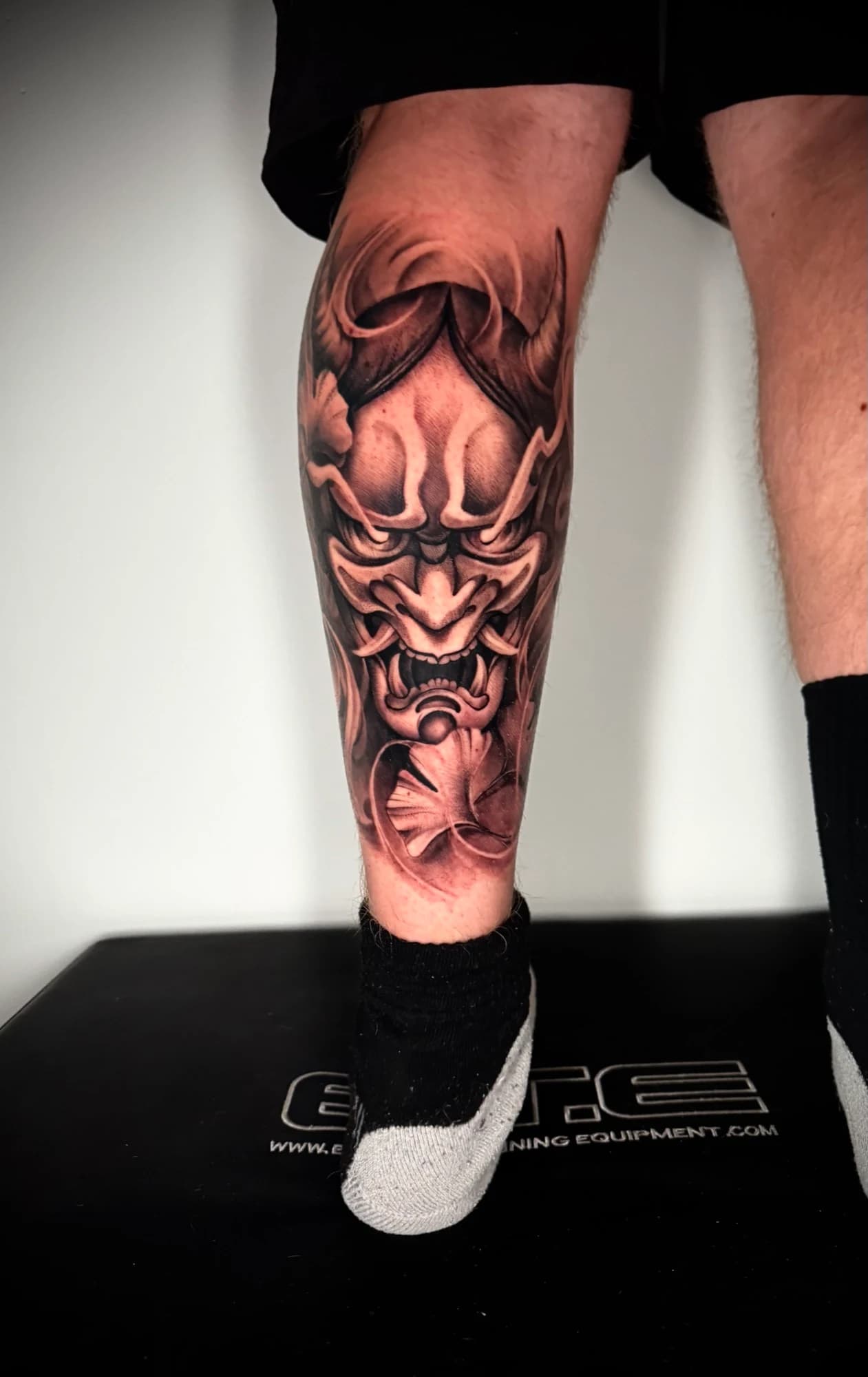 Black and grey tattoo: horned mask with strong contrast and flowing details.