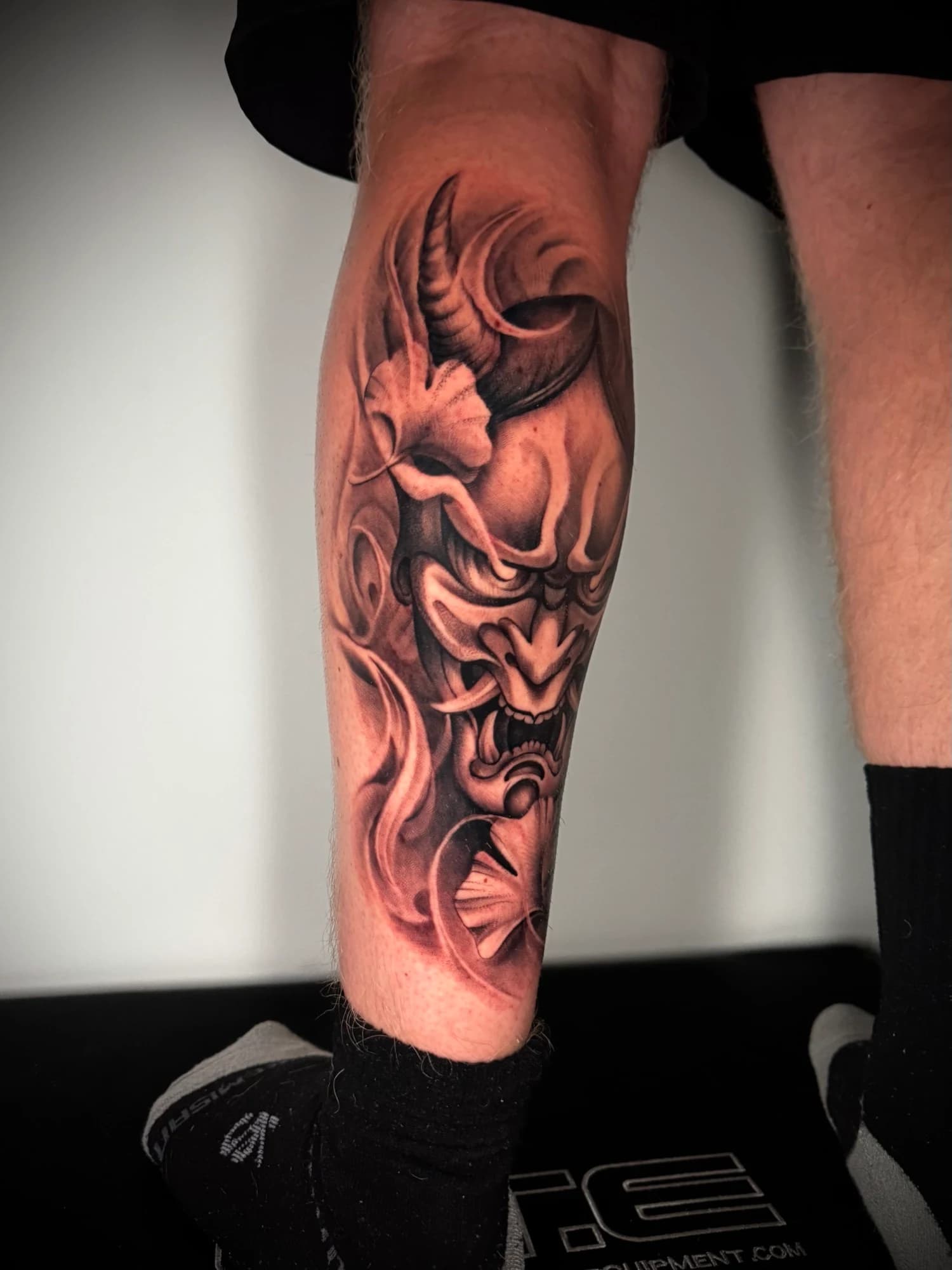Black and grey tattoo: side view of the horned mask and its flowing details.