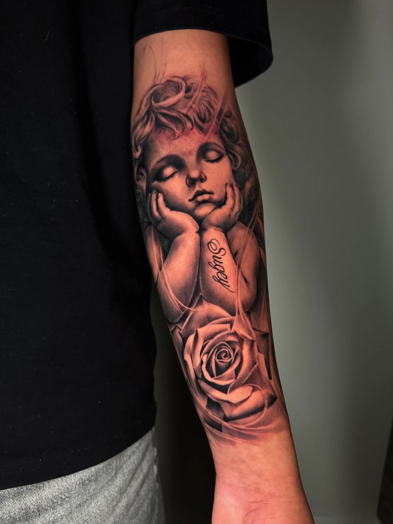 Black and grey tattoo: close view of the cherub and rose forearm tattoo.