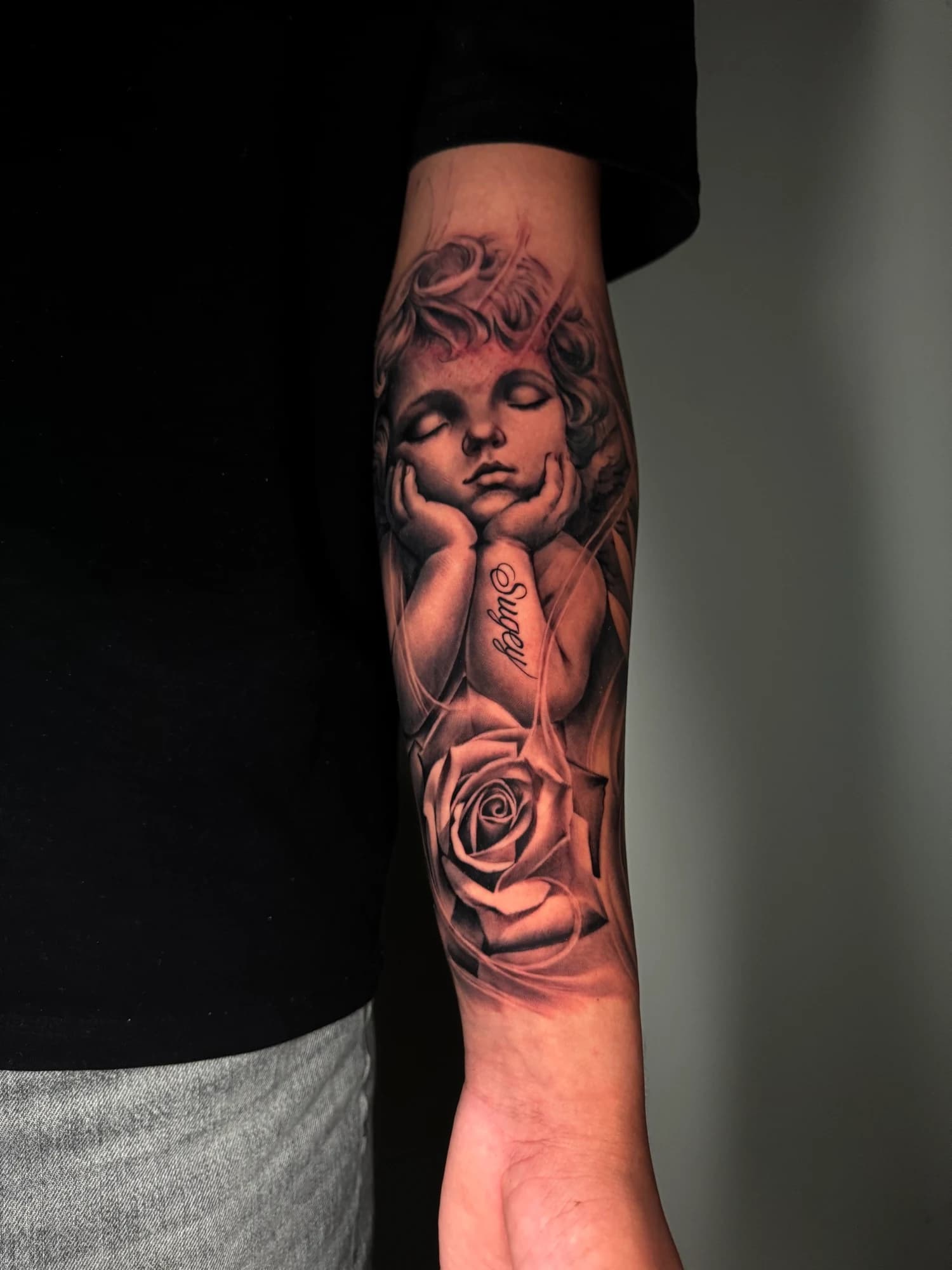 Black and grey tattoo: full view of the cherub and rose composition.