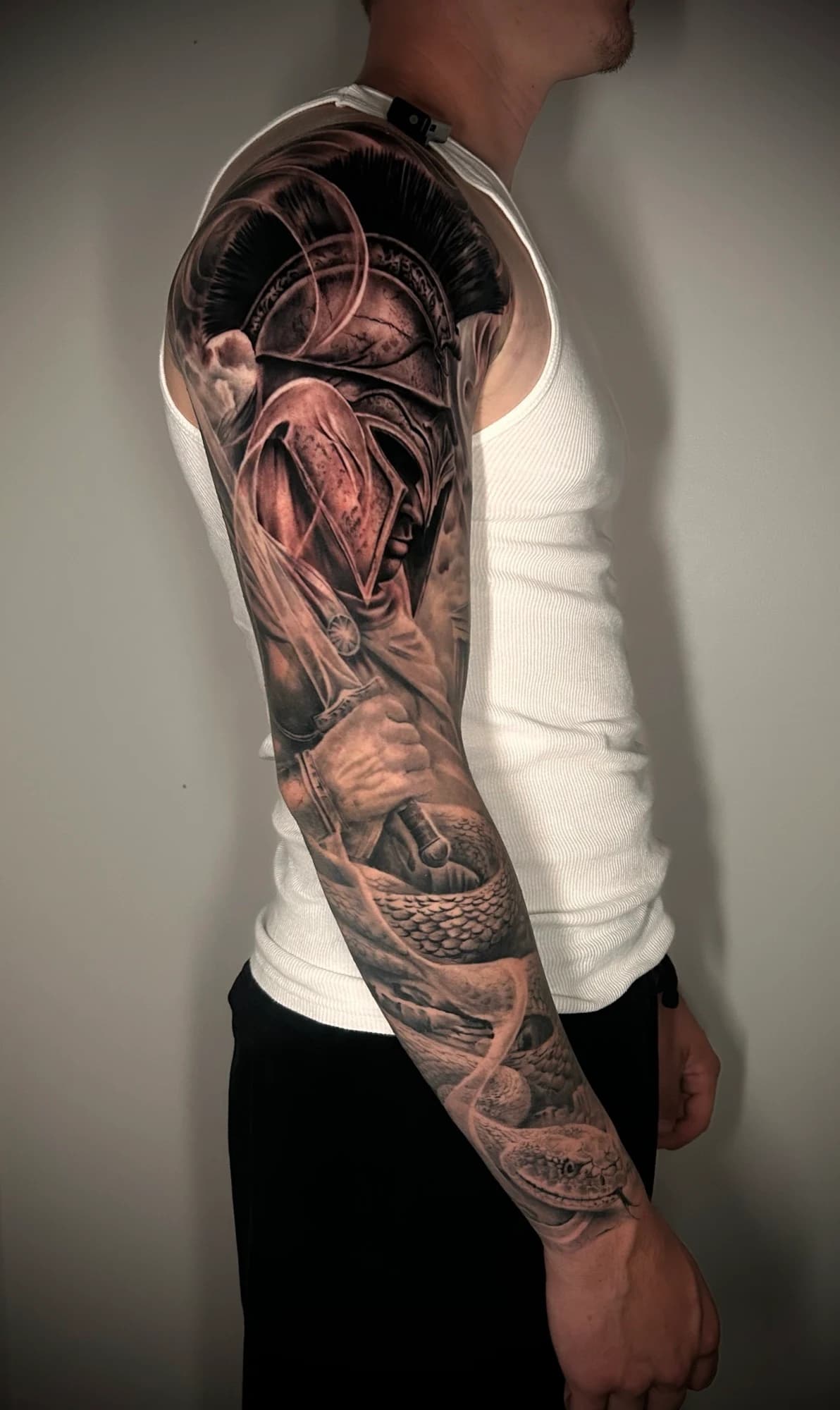 Black and grey tattoo: warrior helmet and architectural details built along the arm.