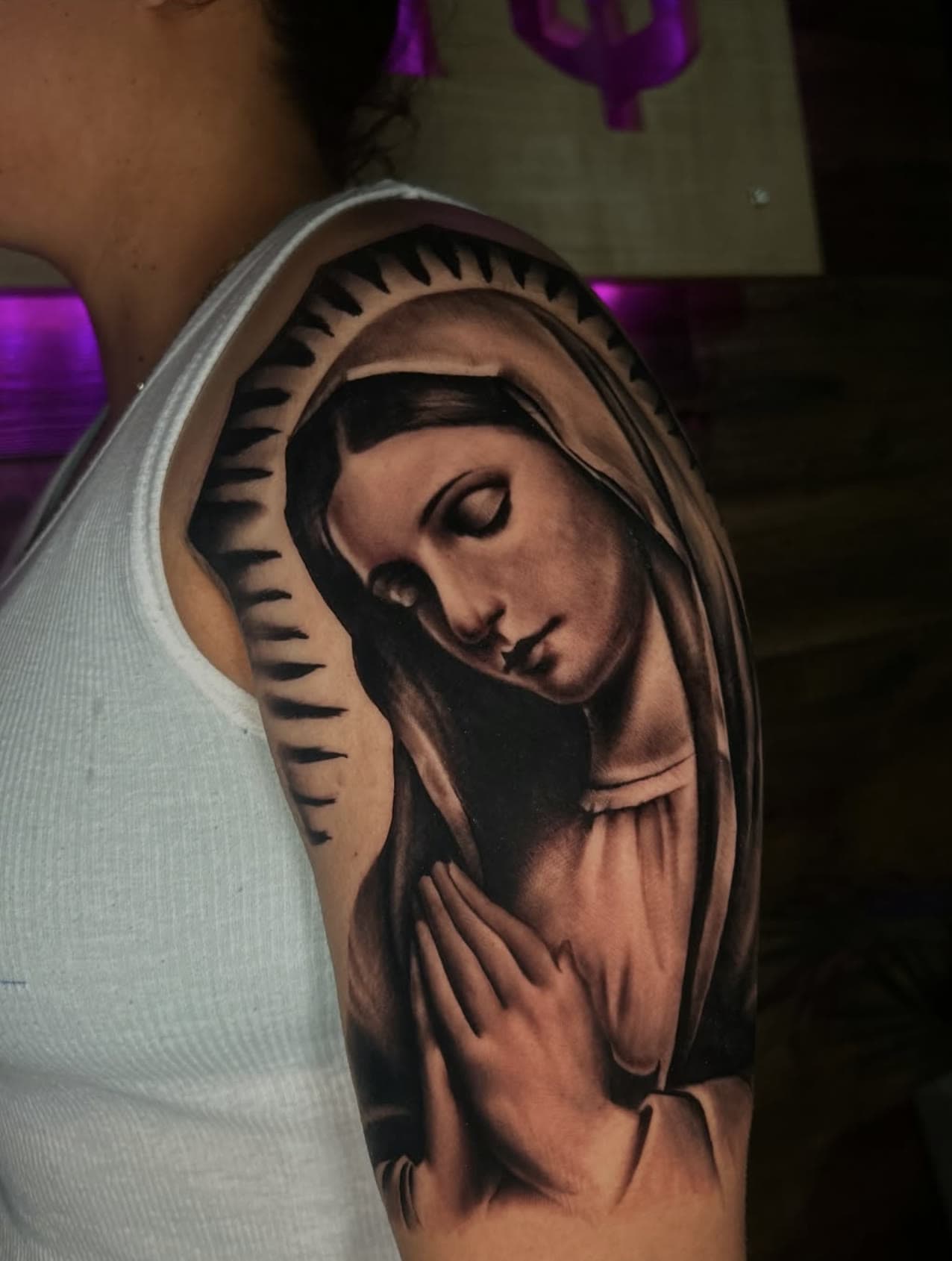 Black and grey Virgin Mary tattoo with halo rays on an upper arm