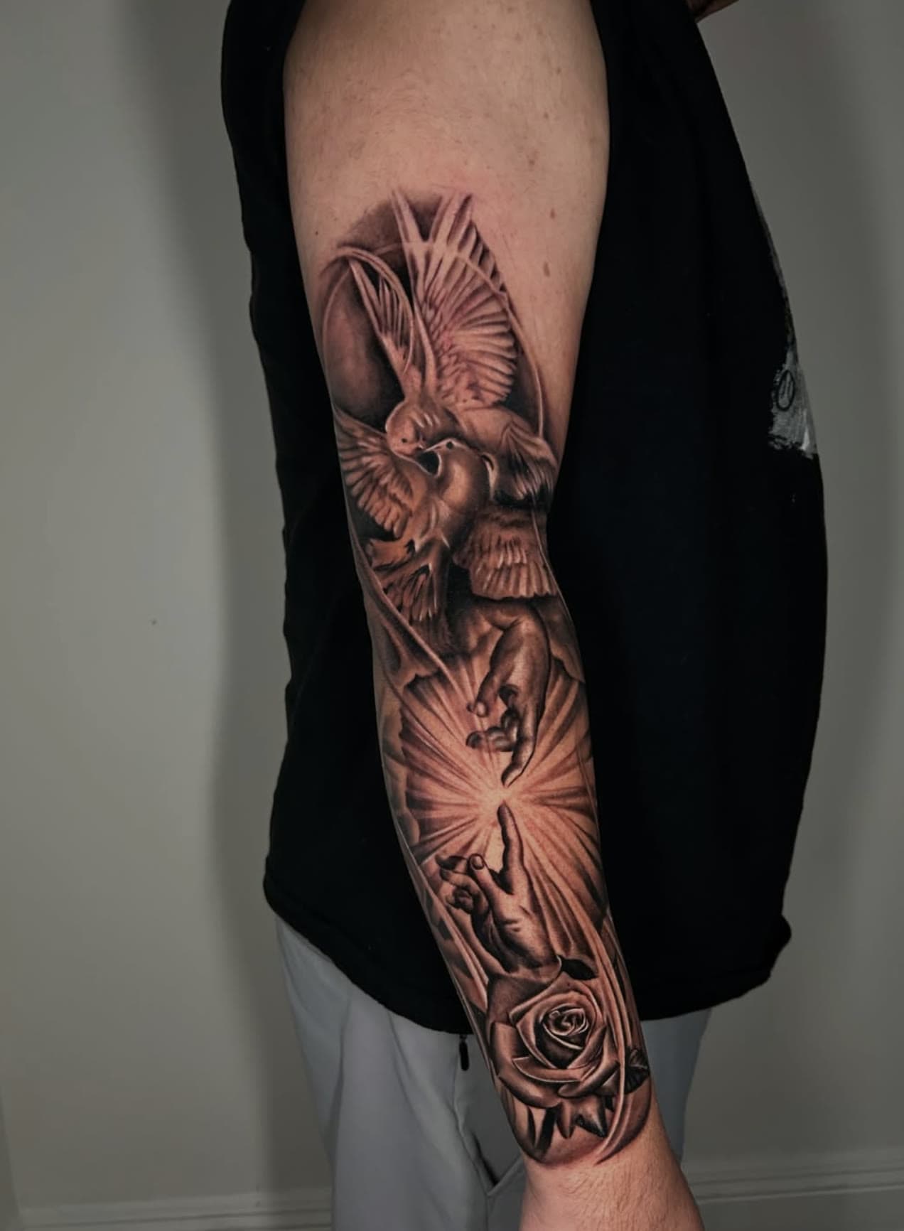Full sleeve in black and grey — an angel with spread wings above a rose and rays of light