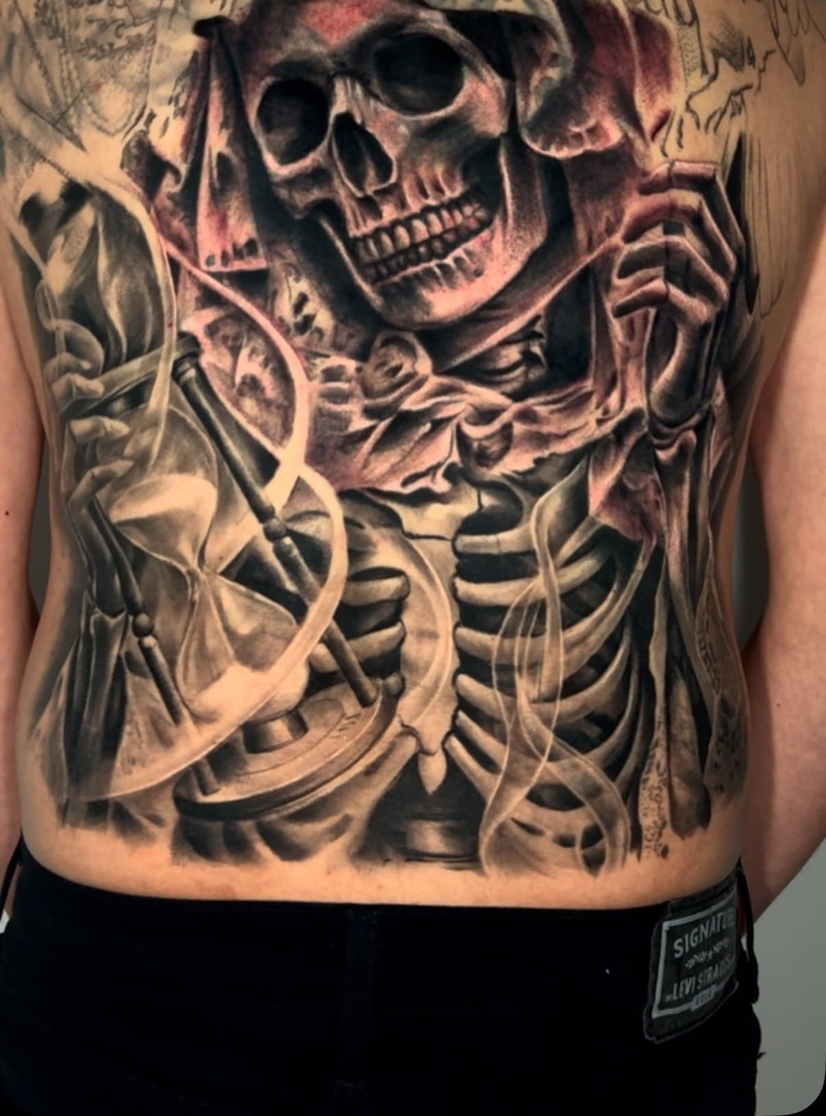 Full back piece in black and grey — a skeletal figure with an hourglass and gears